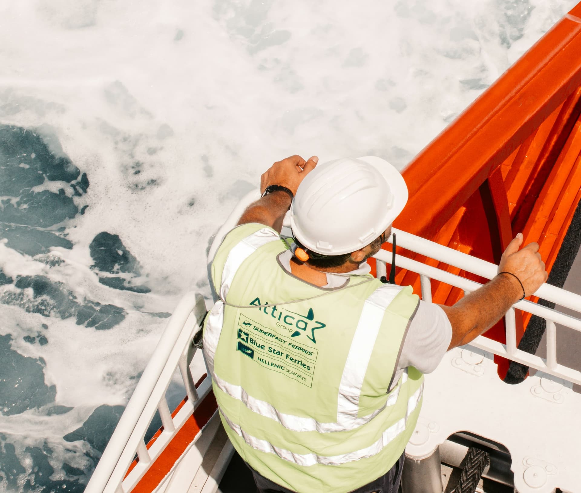 A deckhand in a hard hat and high-visibility vest at the rail, watching the sea